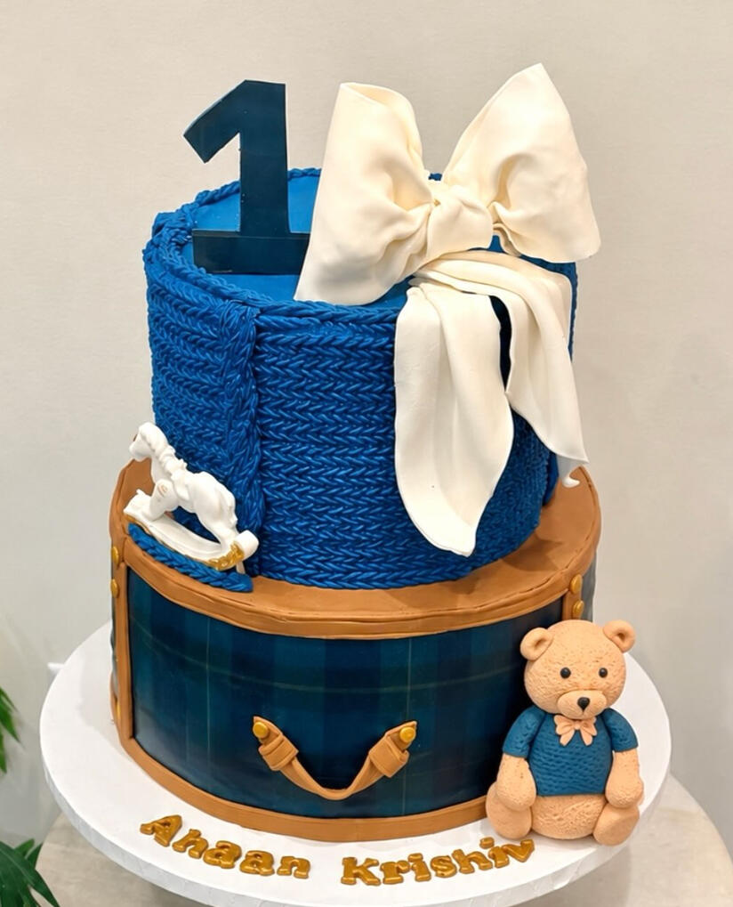 Blue and white first birthday cake with a teddy bear and large number one decoration